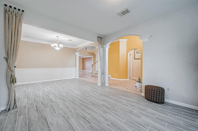 unfurnished living room with crown molding, a chandelier, and ornate columns