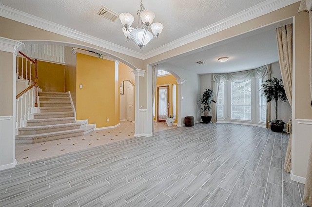 entryway featuring a notable chandelier, ornamental molding, a textured ceiling, and ornate columns