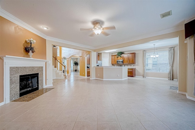 unfurnished living room featuring a tiled fireplace, ornamental molding, ceiling fan with notable chandelier, and light tile patterned floors