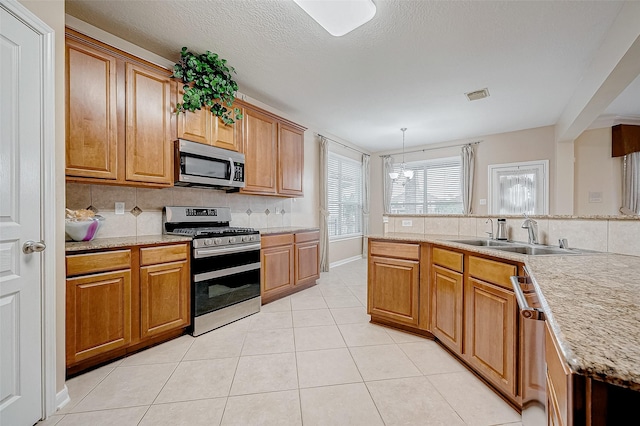 kitchen featuring light tile patterned flooring, sink, decorative light fixtures, appliances with stainless steel finishes, and decorative backsplash