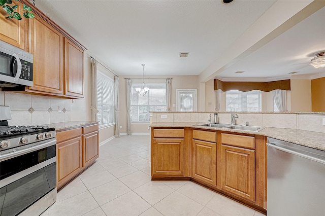 kitchen with appliances with stainless steel finishes, decorative light fixtures, tasteful backsplash, sink, and light tile patterned floors