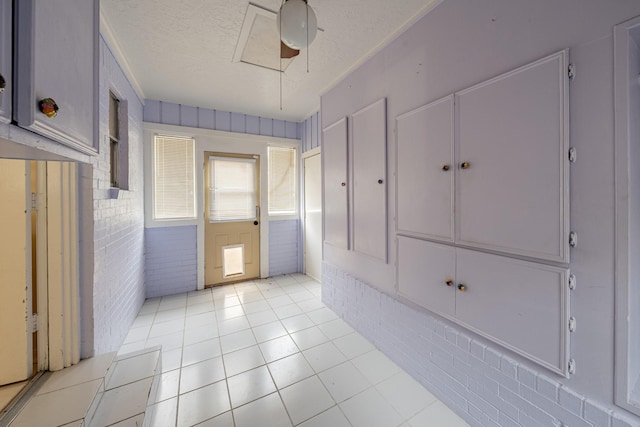 interior space featuring ceiling fan, brick wall, a textured ceiling, and light tile patterned floors