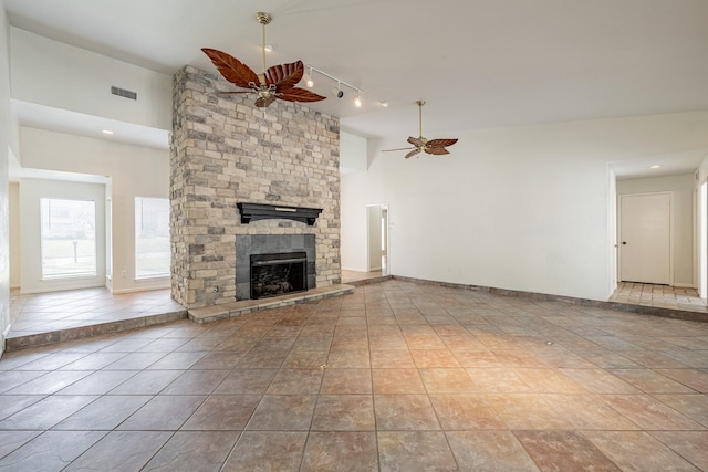 unfurnished living room with light tile patterned flooring, a stone fireplace, ceiling fan, and rail lighting