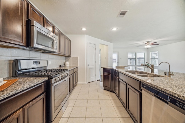 kitchen with sink, light tile patterned floors, appliances with stainless steel finishes, dark brown cabinets, and light stone counters