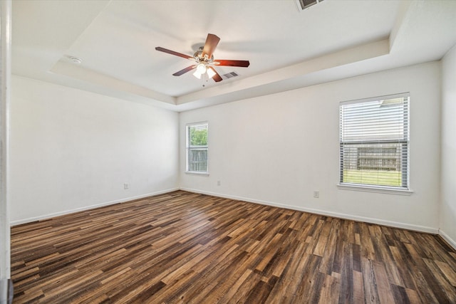 empty room with dark wood-type flooring, ceiling fan, and a tray ceiling