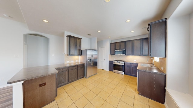 kitchen with sink, dark brown cabinets, appliances with stainless steel finishes, kitchen peninsula, and backsplash