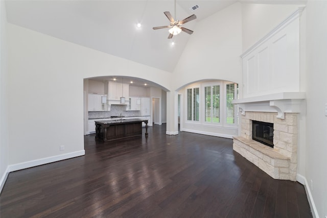 unfurnished living room featuring dark hardwood / wood-style flooring, a fireplace, high vaulted ceiling, and ceiling fan