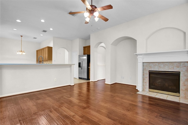 unfurnished living room with sink, ceiling fan with notable chandelier, light hardwood / wood-style flooring, and a tile fireplace