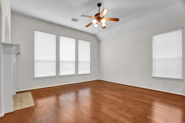 empty room with hardwood / wood-style flooring, ceiling fan, vaulted ceiling, and a tile fireplace