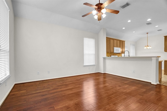 unfurnished living room with ceiling fan with notable chandelier, vaulted ceiling, and dark hardwood / wood-style floors