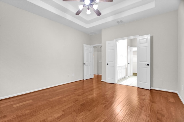 unfurnished bedroom featuring ceiling fan, a raised ceiling, and light hardwood / wood-style flooring