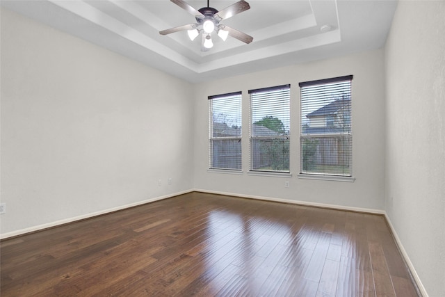 empty room with dark wood-type flooring, ceiling fan, and a raised ceiling