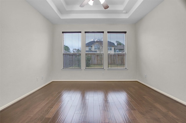 empty room featuring ceiling fan, a healthy amount of sunlight, dark hardwood / wood-style flooring, and a tray ceiling