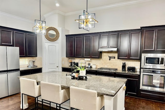 kitchen featuring pendant lighting, light stone countertops, an island with sink, and appliances with stainless steel finishes