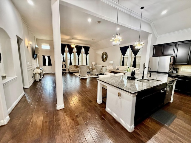 kitchen featuring sink, stainless steel refrigerator, a breakfast bar, light stone counters, and an island with sink