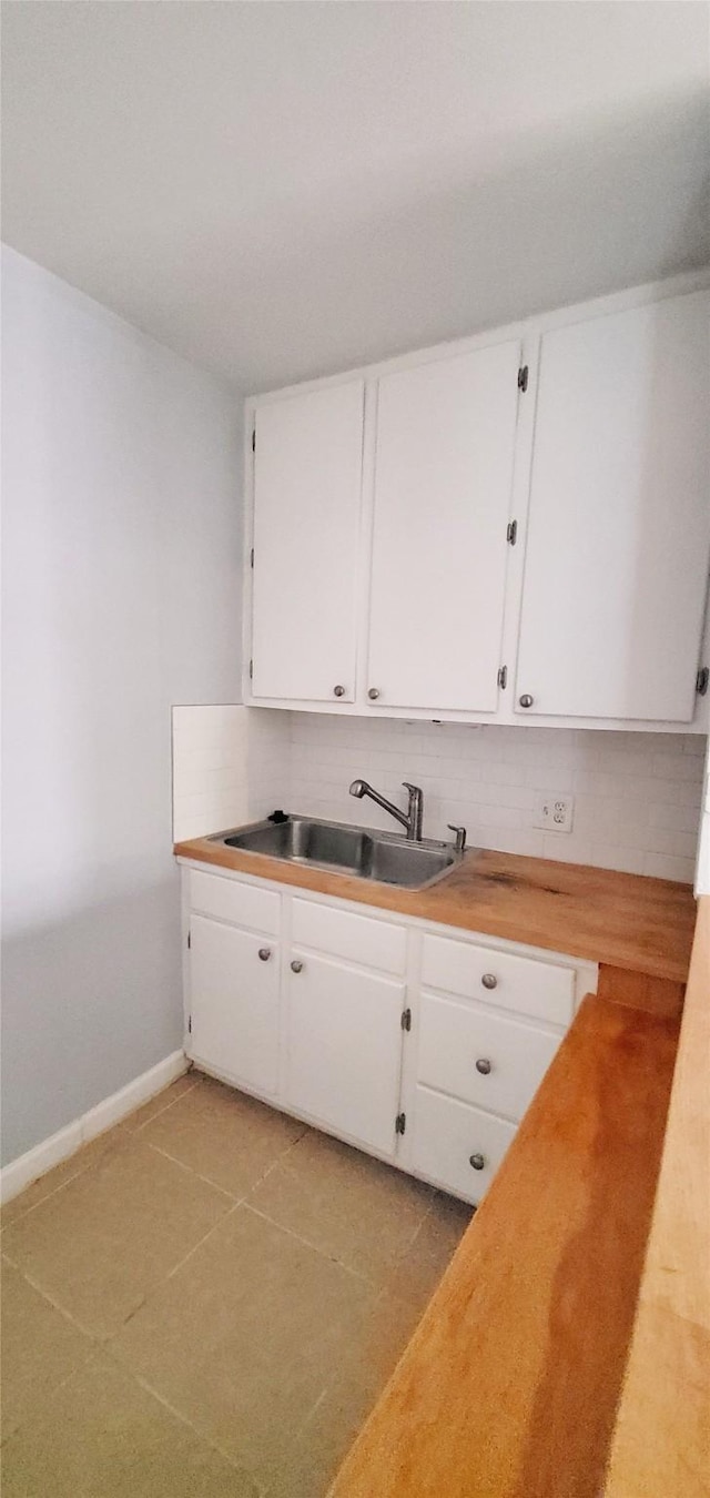 kitchen with light tile patterned flooring, backsplash, sink, and white cabinets