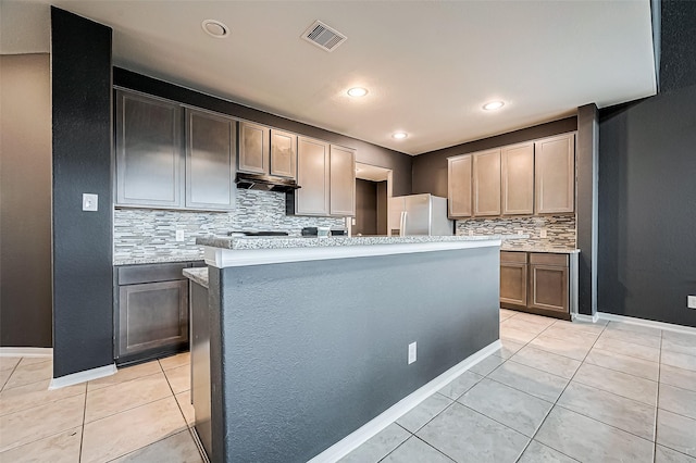 kitchen with tasteful backsplash, a kitchen island, light tile patterned floors, and stainless steel fridge