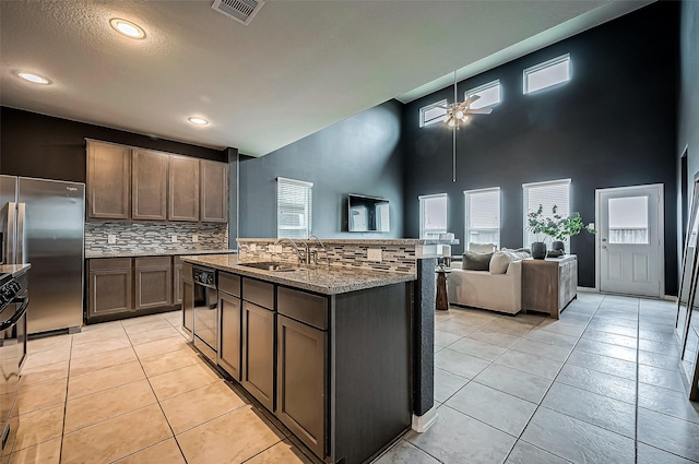 kitchen with tasteful backsplash, stainless steel built in refrigerator, an island with sink, sink, and a high ceiling