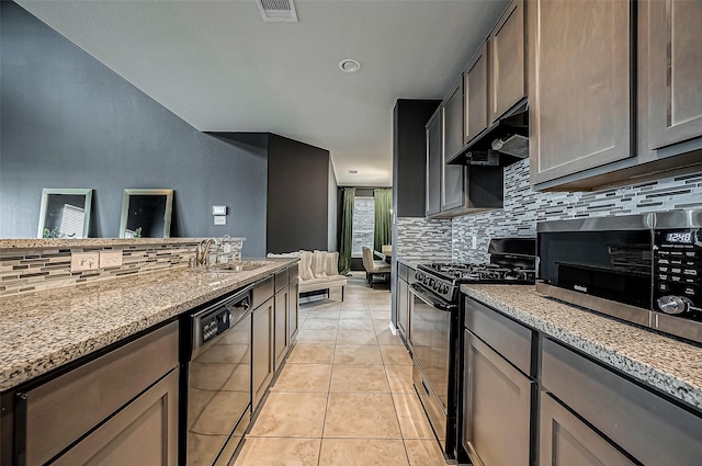 kitchen with sink, decorative backsplash, light tile patterned floors, light stone counters, and black appliances