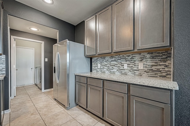 kitchen featuring light tile patterned floors, stainless steel fridge, gray cabinetry, light stone counters, and decorative backsplash