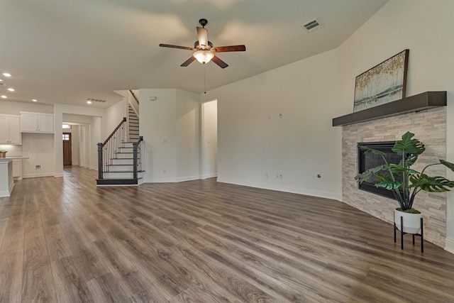 unfurnished living room featuring a stone fireplace, wood finished floors, visible vents, a ceiling fan, and stairway