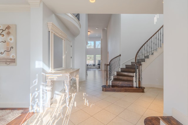 foyer with ornamental molding, a towering ceiling, and light tile patterned floors