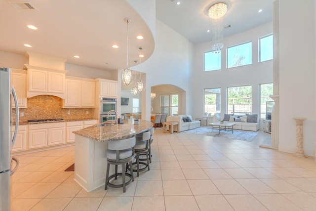 kitchen with hanging light fixtures, stainless steel appliances, light stone countertops, a center island with sink, and decorative backsplash