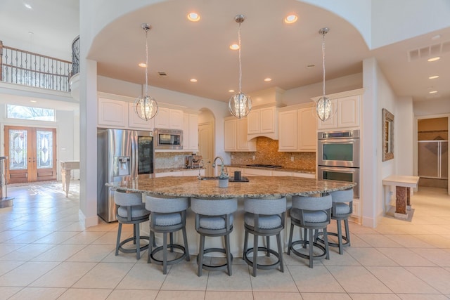 kitchen with light tile patterned floors, dark stone countertops, appliances with stainless steel finishes, an island with sink, and decorative backsplash