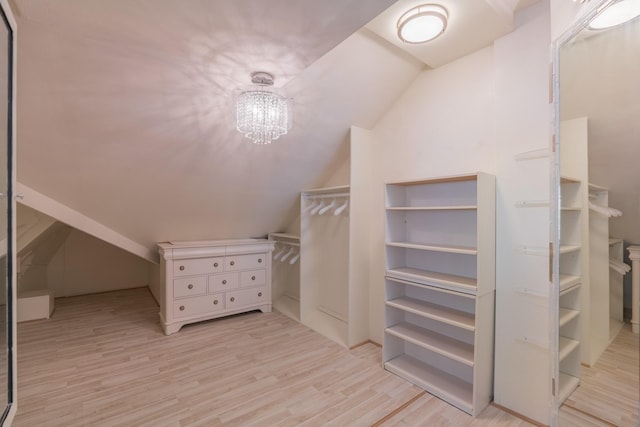 spacious closet with a chandelier, vaulted ceiling, and light wood-type flooring