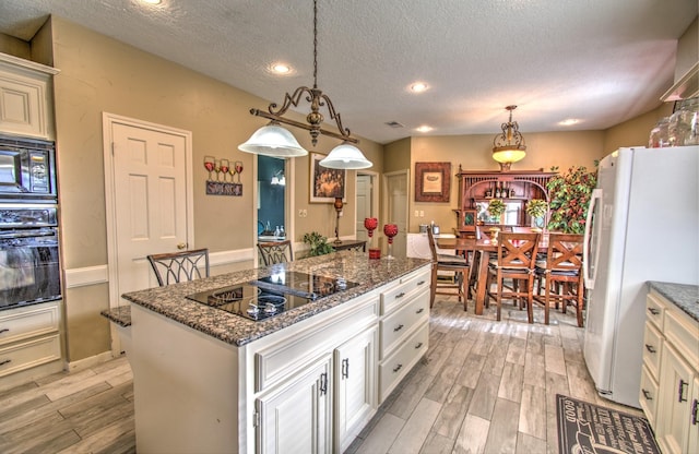 kitchen with light hardwood / wood-style flooring, a center island, black appliances, white cabinets, and decorative light fixtures