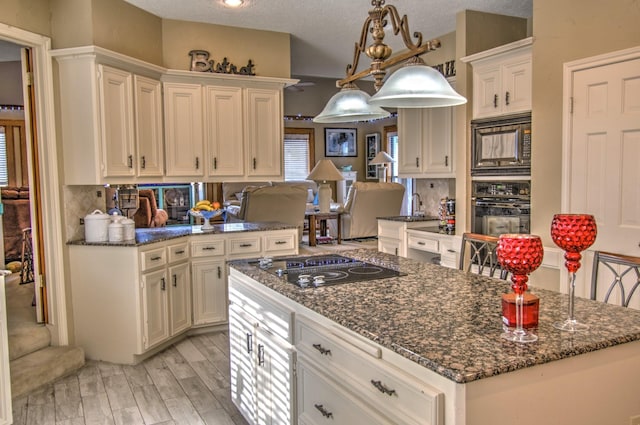 kitchen featuring tasteful backsplash, dark stone countertops, hanging light fixtures, black appliances, and light wood-type flooring