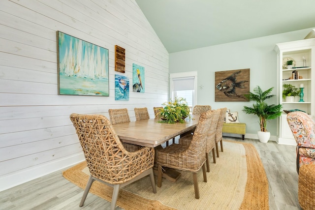 dining area featuring lofted ceiling, wooden walls, and light wood-type flooring