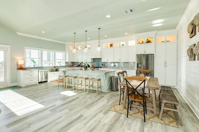 kitchen with pendant lighting, white cabinets, a center island, light stone counters, and stainless steel appliances