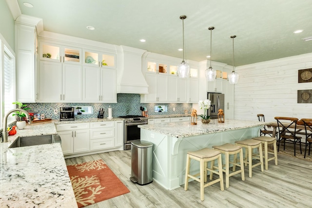 kitchen featuring decorative light fixtures, sink, white cabinets, stainless steel appliances, and custom range hood