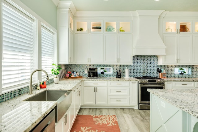 kitchen featuring sink, custom exhaust hood, stainless steel gas stove, white cabinetry, and light stone counters