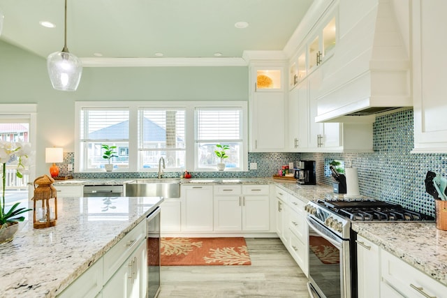 kitchen with sink, custom exhaust hood, stainless steel gas stove, white cabinetry, and decorative light fixtures