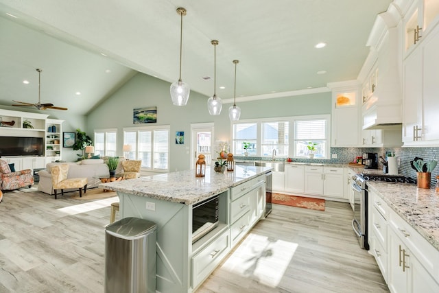 kitchen featuring stainless steel gas range, white cabinetry, light stone counters, a center island, and backsplash