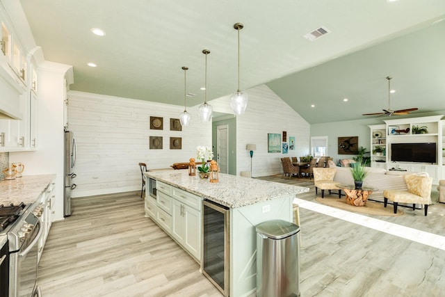 kitchen featuring a kitchen island, pendant lighting, wood walls, white cabinetry, and wine cooler