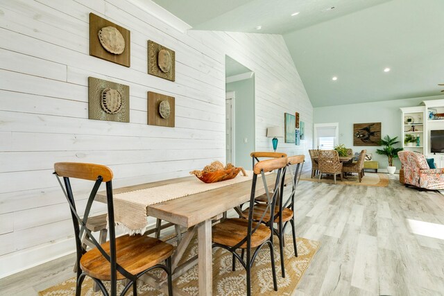 dining area with light hardwood / wood-style floors, vaulted ceiling, and wood walls