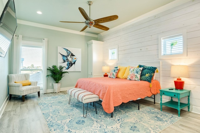 bedroom featuring ceiling fan, ornamental molding, light wood-type flooring, and wood walls