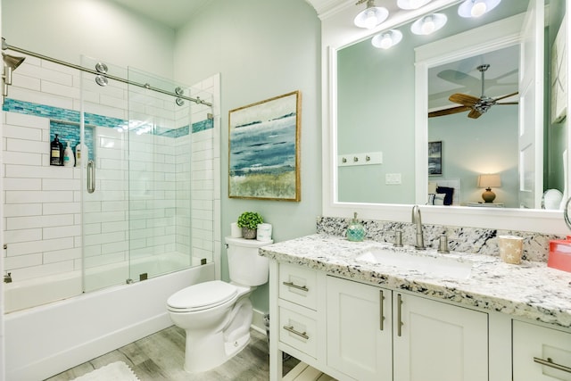 full bathroom with hardwood / wood-style flooring, enclosed tub / shower combo, vanity, ceiling fan, and toilet