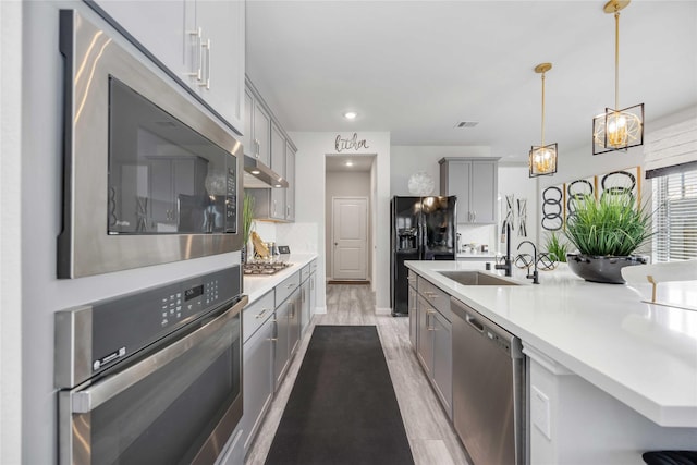 kitchen featuring sink, appliances with stainless steel finishes, gray cabinetry, hanging light fixtures, and light hardwood / wood-style floors