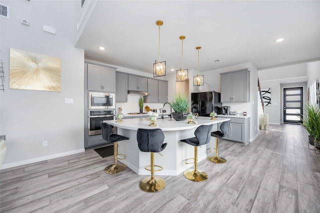 kitchen featuring pendant lighting, appliances with stainless steel finishes, gray cabinetry, a kitchen breakfast bar, and a center island with sink