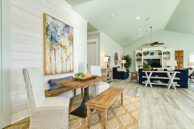 dining room with vaulted ceiling, wooden walls, and light hardwood / wood-style flooring