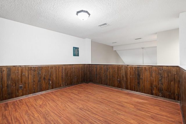 empty room with hardwood / wood-style flooring, a textured ceiling, and wood walls