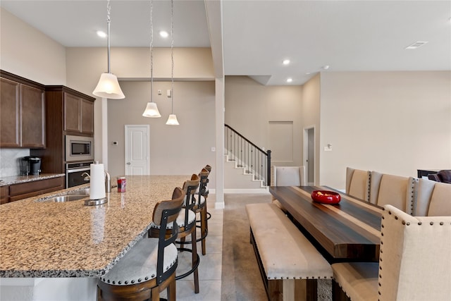 kitchen with a kitchen bar, an island with sink, pendant lighting, stainless steel appliances, and light stone countertops