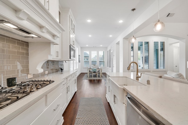 kitchen featuring sink, custom exhaust hood, white cabinetry, hanging light fixtures, and appliances with stainless steel finishes