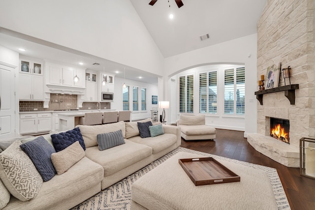 living room with dark hardwood / wood-style flooring, a stone fireplace, high vaulted ceiling, and ceiling fan