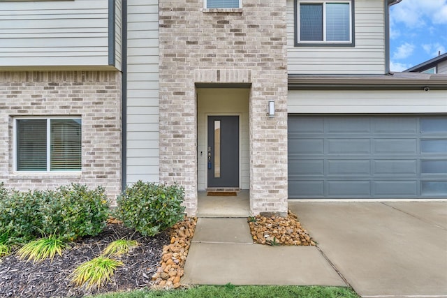 doorway to property with a garage, concrete driveway, and brick siding