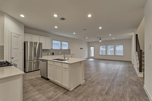 kitchen featuring sink, appliances with stainless steel finishes, a kitchen island with sink, light stone counters, and white cabinets